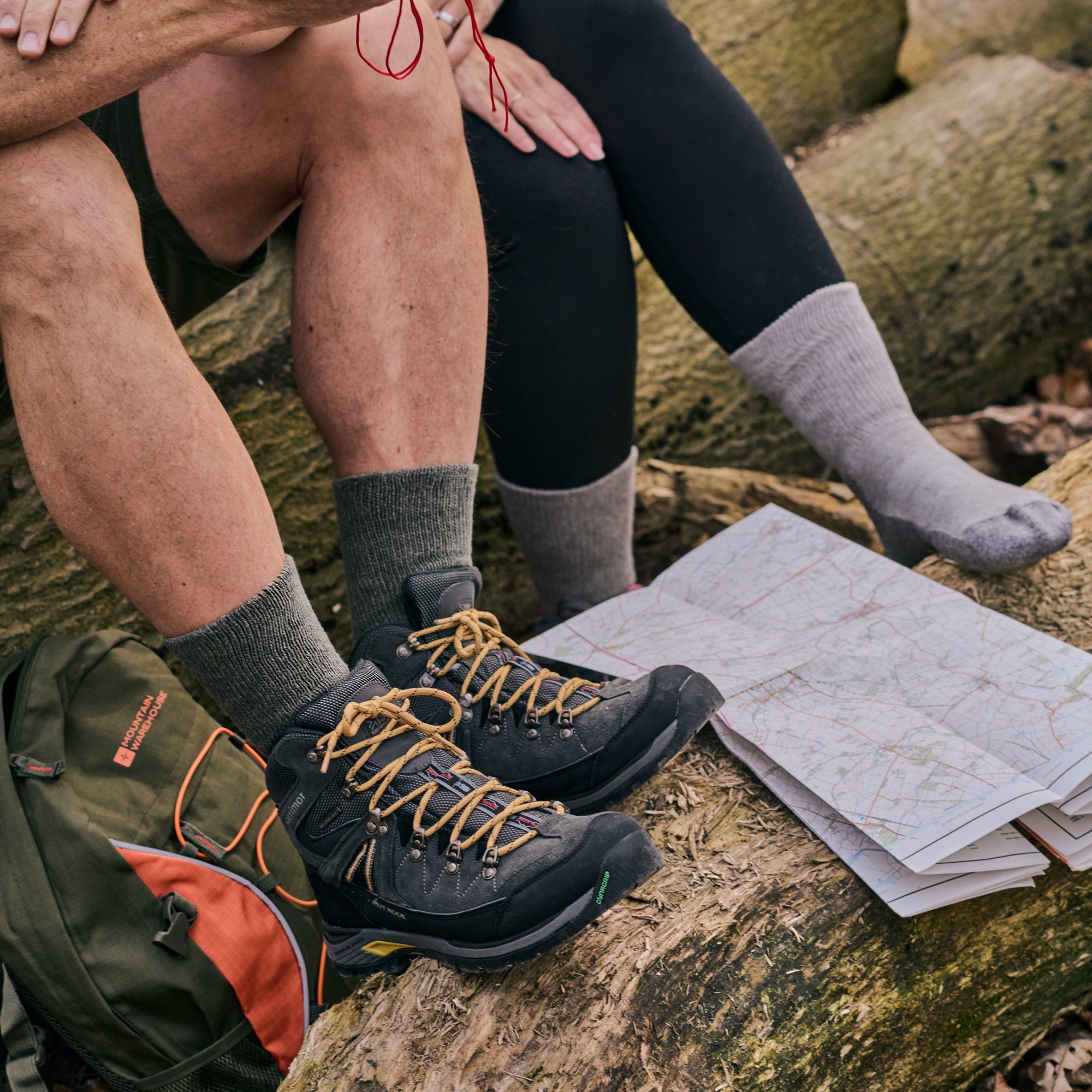 Two people sitting on rocks with hiking socks, boots and a map