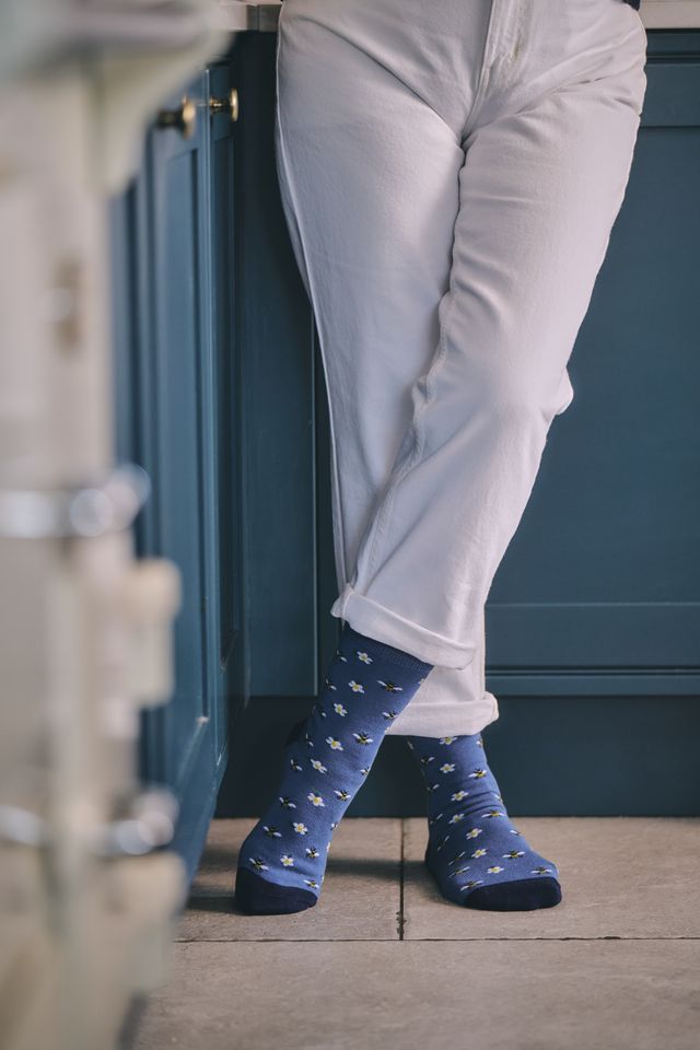 A person wearing white pants and blue socks with a small white pattern, standing in front of dark blue cabinets.