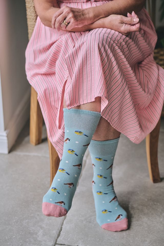A person seated on a chair wearing light blue crew socks with a fish pattern and pink toes and heels, paired with a pink striped dress.