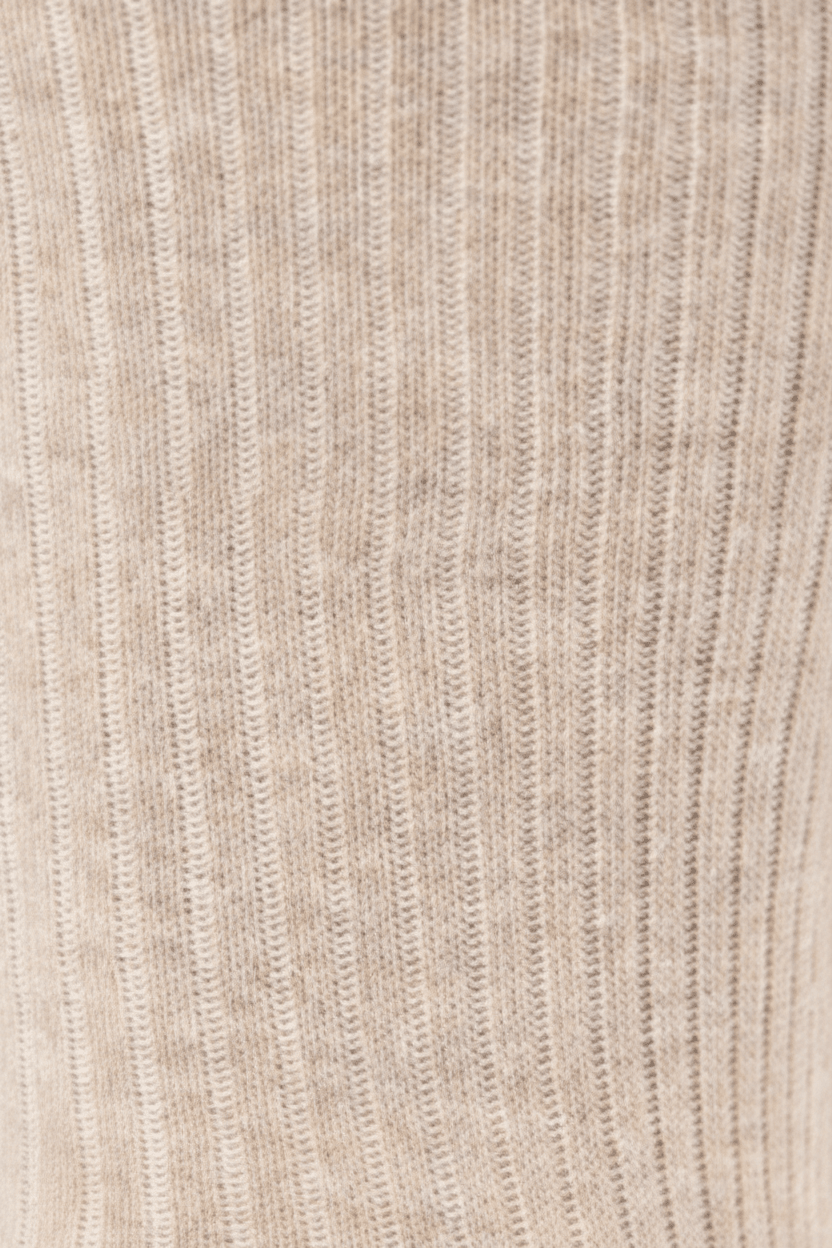 Close-up of a ribbed knit fabric in a warm light beige or oatmeal tone, showing vertical ribbing texture.