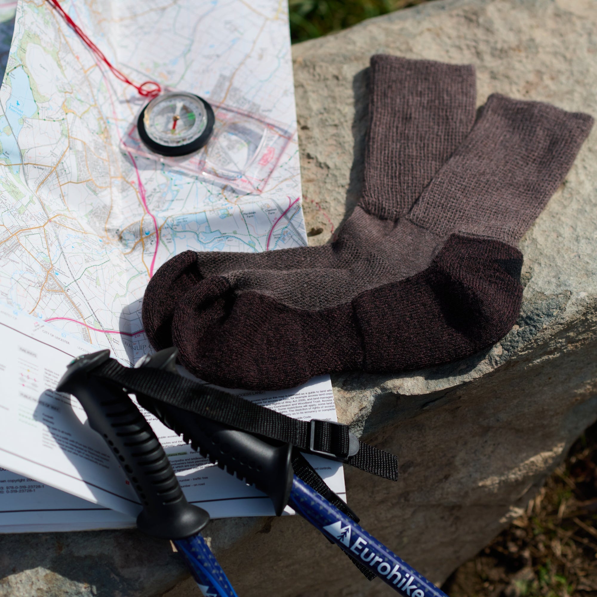 Pair of brown socks on a map with a compass and hiking pole, on a stone surface.