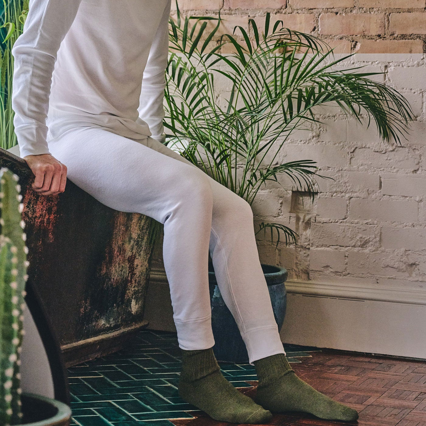 Man sitting on a chair in a room with plants and a brick wall.