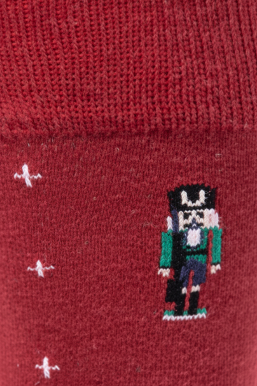 A close-up of a dark red knit sock featuring a small embroidered nutcracker figure and three small white star-like motifs on the side.