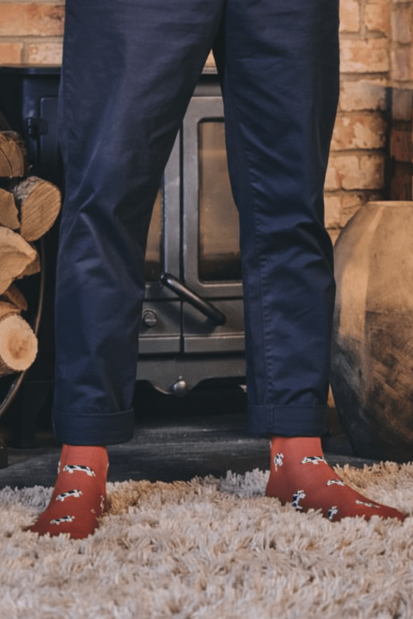 A person standing in front of a fireplace wearing navy pants and rust-red socks with a white pattern, standing on a shag rug.