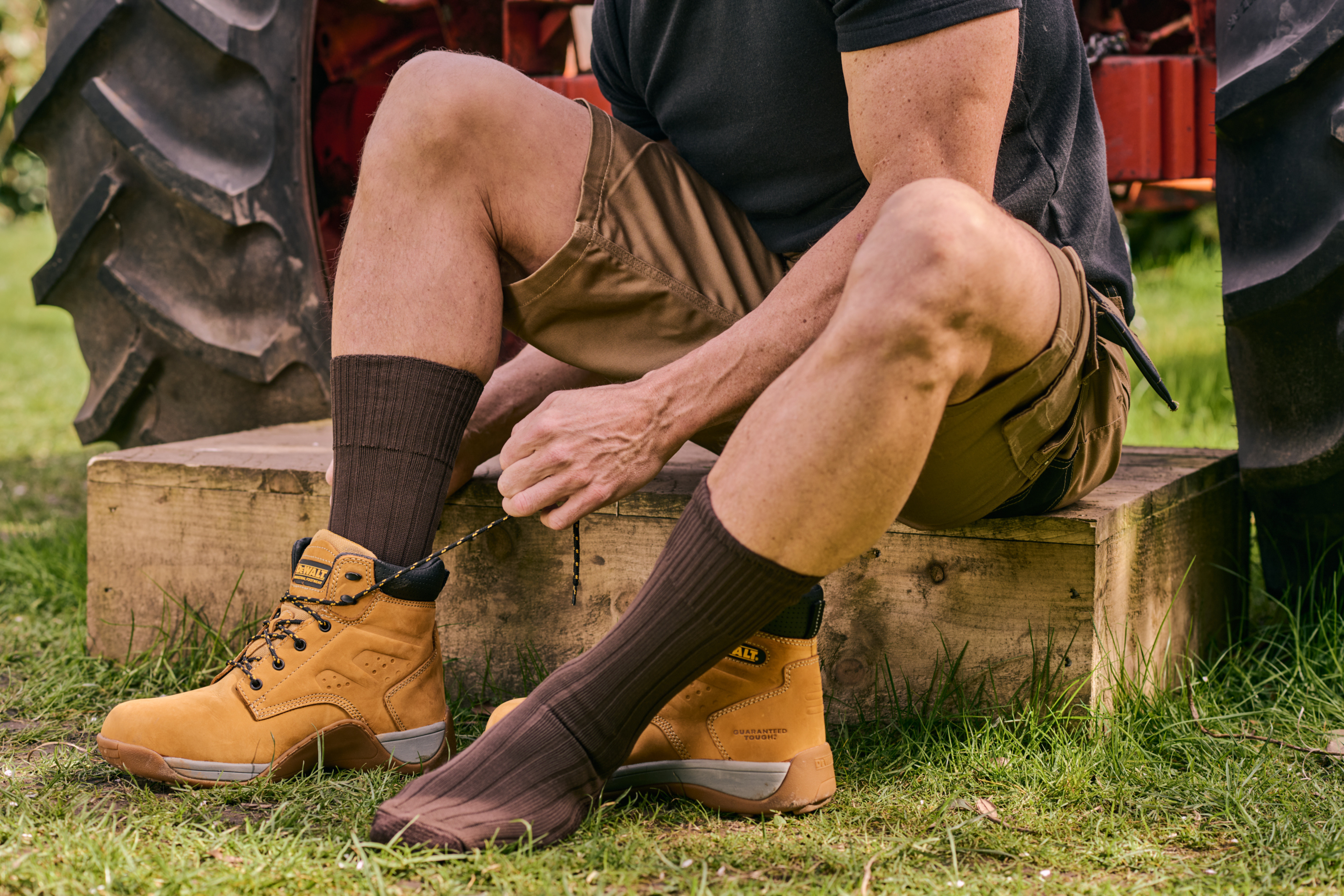 Person wearing brown socks and tan boots sitting on a wooden block outdoors.