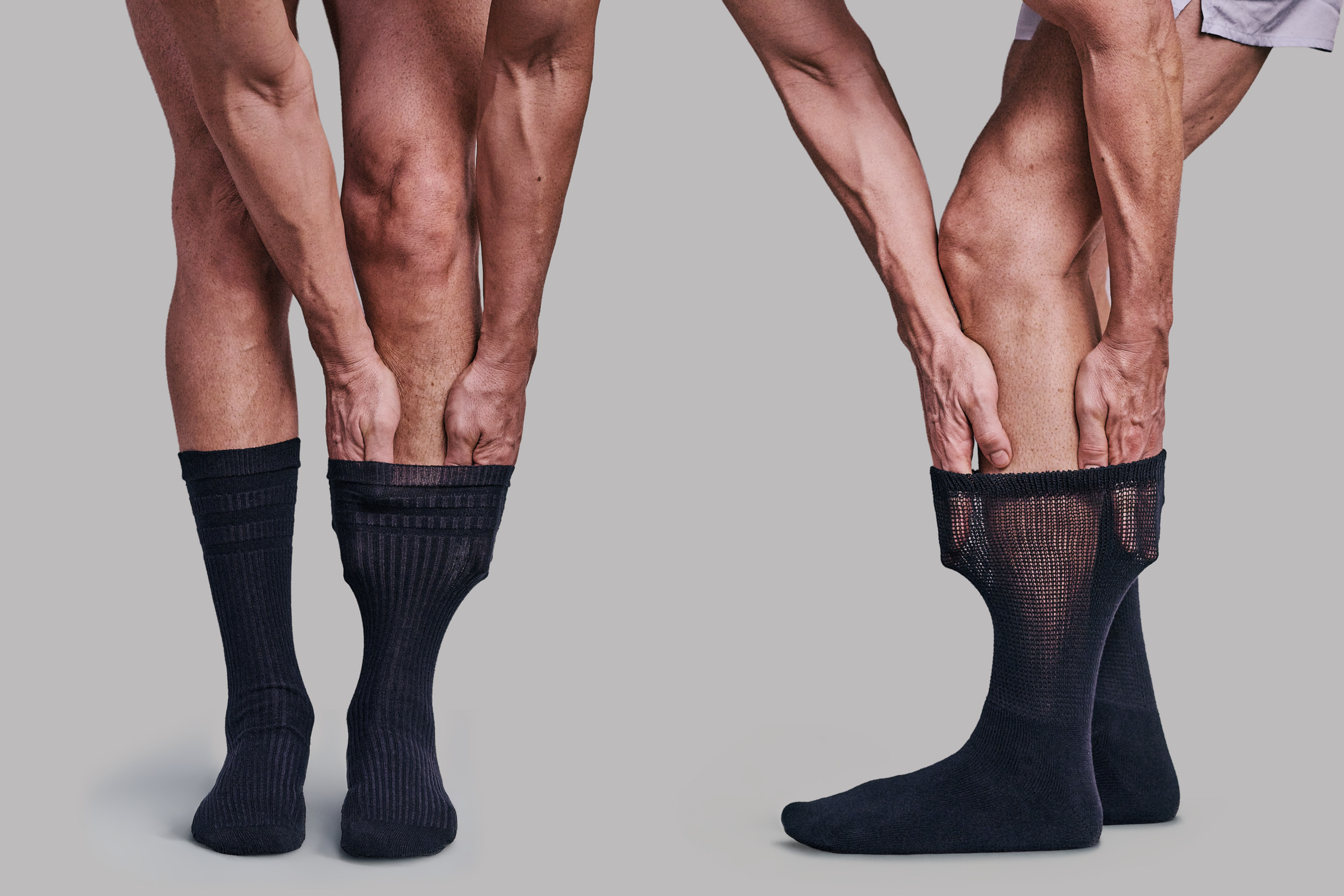 Two pairs of legs wearing black stretchy health socks against a grey background